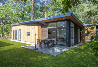 Moderne tiny house ved Bospark 't Wolfsven, Holland, med stor glasfacade og terrasse i grønne omgivelser.