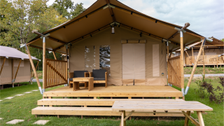 Tente safari Comet 27 Lodges avec terrasse couverte, sièges extérieurs et table de pique-nique sur herbe.