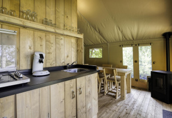 Interieur van de Comet 27 Lodges safaritent in Arden Parks, met houten keuken, eettafel en kachel.