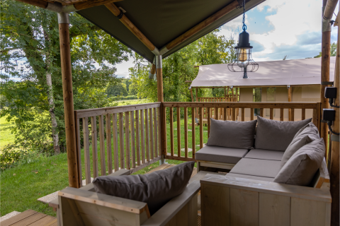Blick von der überdachten Terrasse mit Sofas am Ranger Lodge Safarizelt in Arden Parks, Frankreich.