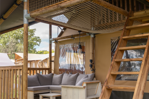 Gemütliche Sitzgruppe mit Holzmöbeln, Kissen und Holzleiter in einem Safari-Zelt der Ranger Lodge in Frankreich.