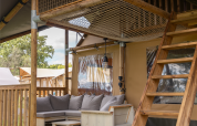 Gemütliche Sitzgruppe mit Holzmöbeln, Kissen und Holzleiter in einem Safari-Zelt der Ranger Lodge in Frankreich.