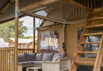 Zona lounge esterna con divanetti in legno, cuscini e scala in una tenda safari Ranger Lodge a Signy l'Abbaye.