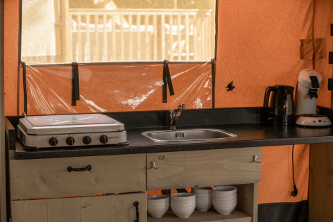 Küchenzeile im Ranger Lodge Safarizelt mit Herd, Spüle, Kaffeemaschine und Schalen.