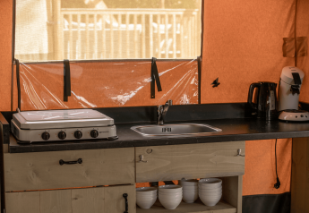 Angolo cucina in tenda safari Ranger Lodge con fornello, lavello, macchina da caffè e ciotole.
