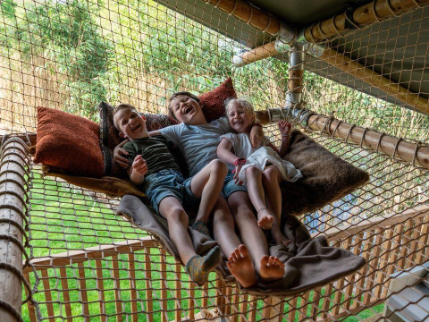Drei lachende Kinder entspannen auf einem Netz mit Kissen im Safari-Zelt Ranger Lodge in Signy l'Abbaye, Frankreich.