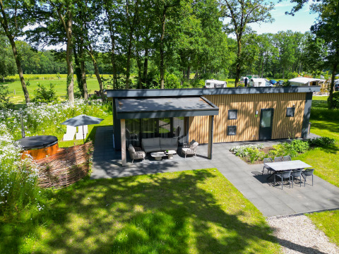 Moderne træhytte, omgivet af grøn natur, med terrasse, boblebad og spisebord i haven ved Wood Cottage.