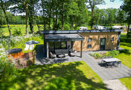 Moderne træhytte, omgivet af grøn natur, med terrasse, boblebad og spisebord i haven ved Wood Cottage.