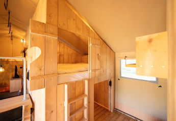 Vista interior de la tienda Safari 6 en Lauwersmeer, Países Bajos, con muebles de madera y litera elevada.