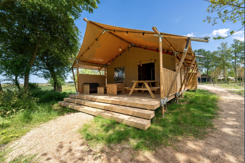 La tienda Safari 8 en Lauwersmeer, Países Bajos, cuenta con terraza de madera y entorno natural verde.