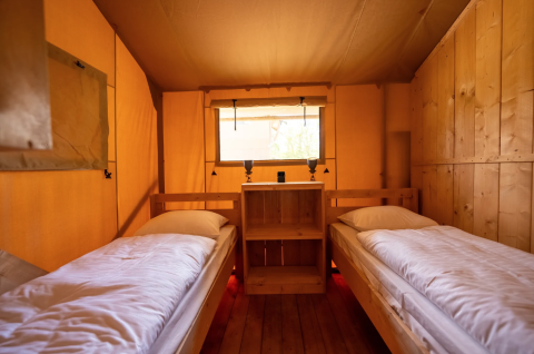 Interior de la tienda Safari 8 en Lauwersmeer, Países Bajos, con dos camas individuales y paredes de madera.