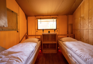Interior de la tienda Safari 8 en Lauwersmeer, Países Bajos, con dos camas individuales y paredes de madera.