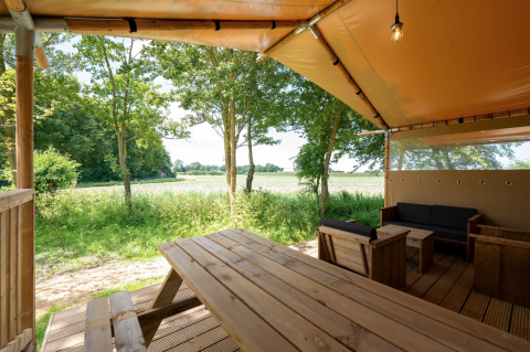 Vista desde la tienda Safari 8 en Lauwersmeer, Países Bajos, con bancos, árboles y campo verde.