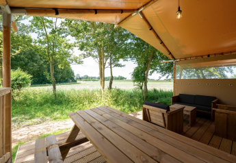 Vista desde la tienda Safari 8 en Lauwersmeer, Países Bajos, con bancos, árboles y campo verde.