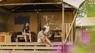 Famiglia che si rilassa davanti alla tenda Safari 8 al Lauwersmeer nei Paesi Bassi, atmosfera accogliente.