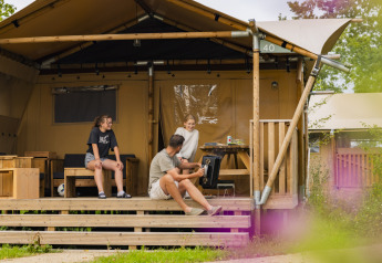 Familia relajándose frente a la tienda Safari 8 en Lauwersmeer, Países Bajos, disfrutando de la naturaleza.