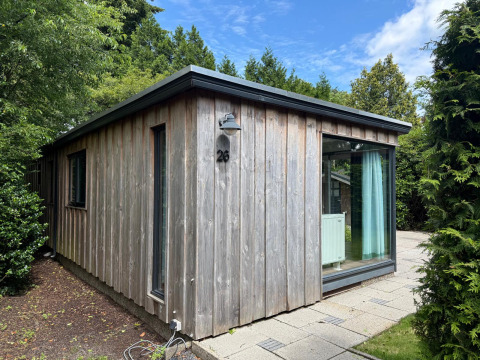 Außenaufnahme der Private Lodge Nummer 26 mit Holzverkleidung und großen Fenstern im Grünen.