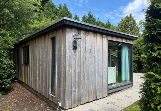 Außenaufnahme der Private Lodge Nummer 26 mit Holzverkleidung und großen Fenstern im Grünen.