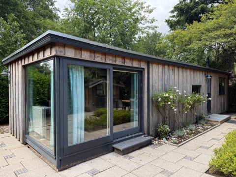 Moderne houten lodge met grote ramen, omgeven door groen in Het Verscholen Dorp, Nederland.