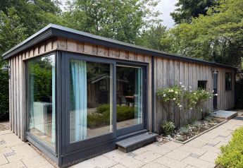 Moderne houten lodge met grote ramen, omgeven door groen in Het Verscholen Dorp, Nederland.