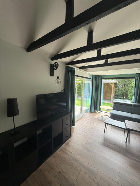 Soggiorno moderno in una lodge con travi nere, porte in vetro e vista sul giardino nei Paesi Bassi.