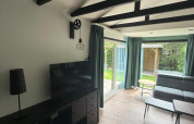 Modernes Wohnzimmer in einer Lodge mit schwarzen Deckenbalken, Glastüren und Gartenblick in den Niederlanden.