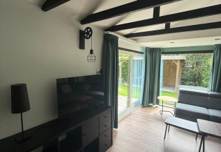 Moderne woonkamer in een lodge met zwarte balken, glazen deuren en zicht op de tuin in Nederland.