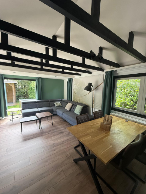 Woonruimte in de «Private» Lodge te Het Verscholen Dorp, Nederland, met moderne hoekbank en houten tafel.