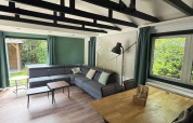 Wohnbereich in der «Private» Lodge bei Het Verscholen Dorp, Niederlande, mit moderner Couch und Holztisch.