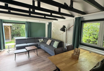 Stue i «Private» Lodge ved Het Verscholen Dorp, Holland, med moderne sofa, træbord og udsigt til natur.