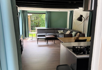 Indgangen til en lys, moderne lodge med åbent køkken og stue, store vinduer og grønne gardiner.