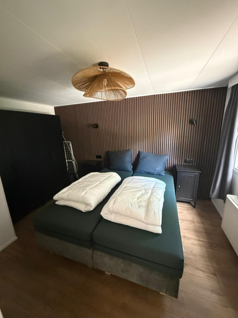 Slaapkamer in de «Private» Lodge bij Het Verscholen Dorp, Nederland, met modern bed en houten wand.