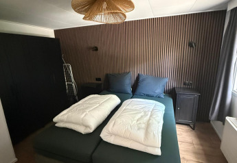 Slaapkamer in de «Private» Lodge bij Het Verscholen Dorp, Nederland, met modern bed en houten wand.
