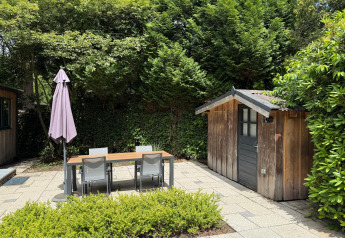 Hyggelig terrasse med spisebord, havestole og et lille træskur hos ‘Private’ Lodge, Het Verscholen Dorp.