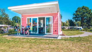 Familia relajándose frente a Valley Chalet, una tiny house rosa en Holiday park Ackersate, Países Bajos.