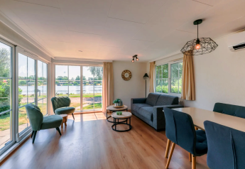 Lyst opholdsområde i Chalet 4 ved Tolplas, Nederlandene, med store vinduer og udsigt over søen.