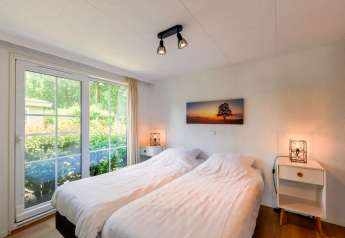 Chambre lumineuse du Chalet 4 à Tolplas, Pays-Bas, avec deux lits et grande baie vitrée sur le jardin.