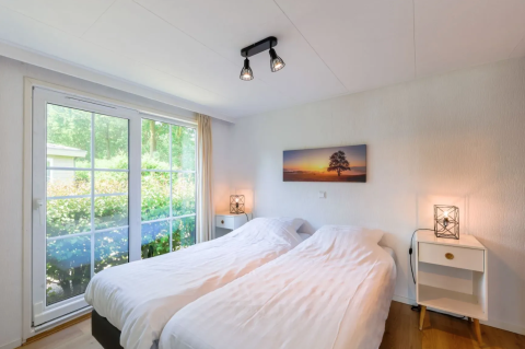 Helles Schlafzimmer im Chalet 4 in Tolplas, Niederlande, mit zwei Betten und großem Fenster zum Garten.
