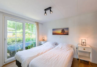 Helles Schlafzimmer im Chalet 4 in Tolplas, Niederlande, mit zwei Betten und großem Fenster zum Garten.