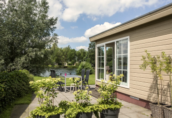 Udsigt over Chalet 4 ved Tolplas i Holland med terrasse, havemøbler, solskin og fredelig sø.