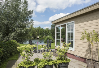 Udsigt over Chalet 4 ved Tolplas i Holland med terrasse, havemøbler, solskin og fredelig sø.