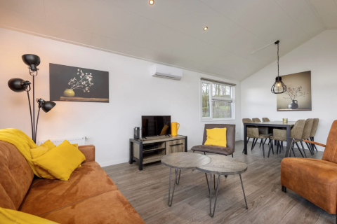 Sala de estar en la cabaña Schipbeek 6 en Tolplas, Países Bajos, con muebles modernos y detalles amarillos.