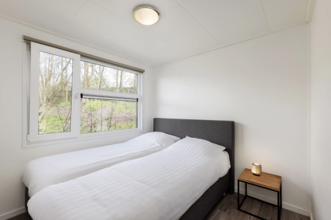 Slaapkamer van Schipbeek 6 lodge bij Tolplas, Nederland, met twee single bedden en een groot raam.
