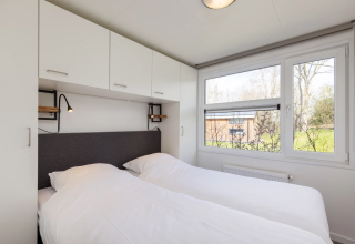 Schlafzimmer in der Lodge Schipbeek 6 in Tolplas, Niederlande, mit Doppelbett und Panoramafenstern.