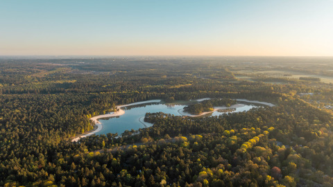 Luchtfoto van een lodge aan een meer, omgeven door dicht bos en natuurschoon in avondlicht.