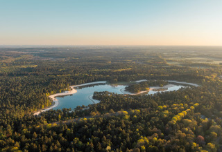 Luchtfoto van een lodge bij een meer, omringd door dichte bossen en natuur in de avondzon.