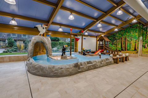 Binnen kinderbad met dierfiguren, glijbaan en speelgedeelte in een modern lodge met boswanddecor.