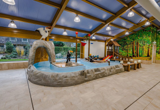 Binnen kinderbad met dierfiguren, glijbaan en speelgedeelte in een modern lodge met boswanddecor.