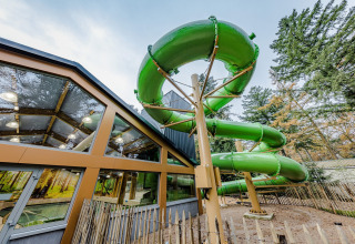 Grote groene schuifaf naast een modern lodgegebouw, omringd door bomen en een houten afsluiting.