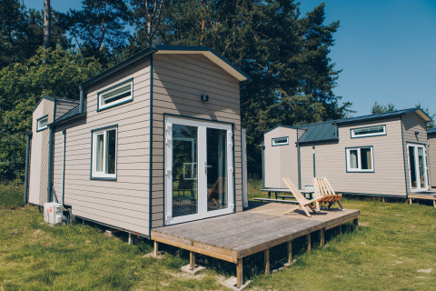 A photo of the 'Koya Tiny Loft' tiny houses at Wilsumer Berge, Germany, featuring wooden decks and trees.